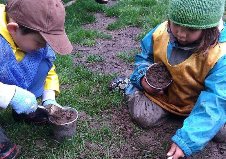 Two children are playing with dirt in the grass.