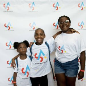 Three children posing for a picture in front of a wall.