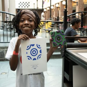 A young girl holding up a paper and a mandala.
